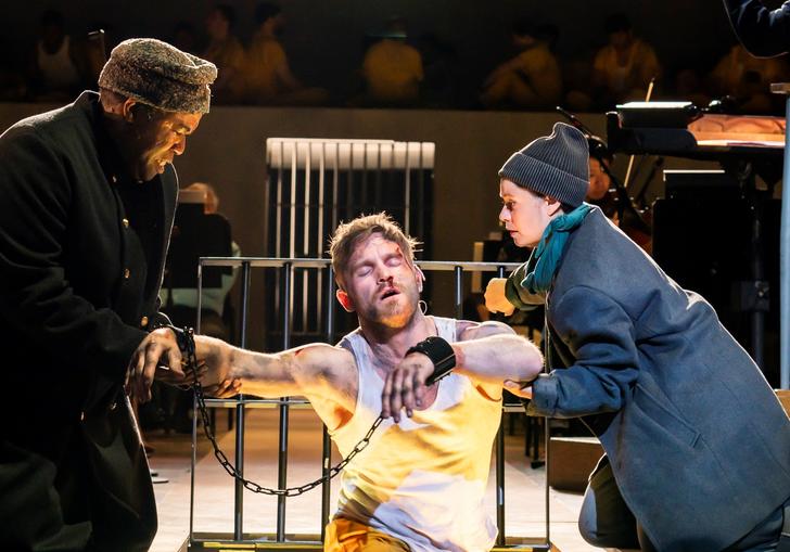 A jailer and his assistant helping a prisoner in chains out of cell