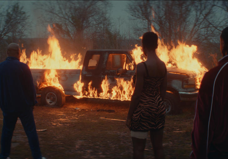 people standing in front of a burning car