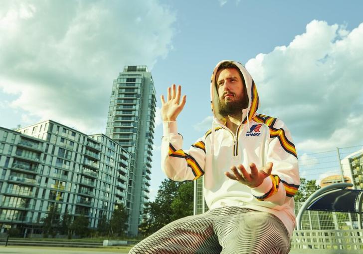 Danalogue sitting amongst glass buildings, gesturing with his hands