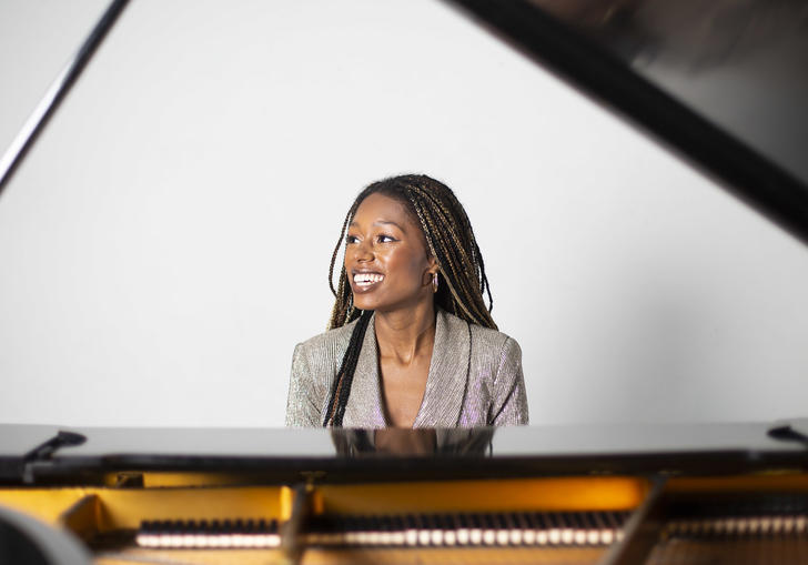 Am image of Isata sitting by the piano and smiling