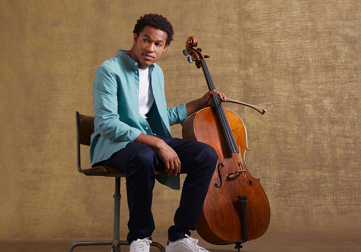 Sheku sitting on a chair holding his cello