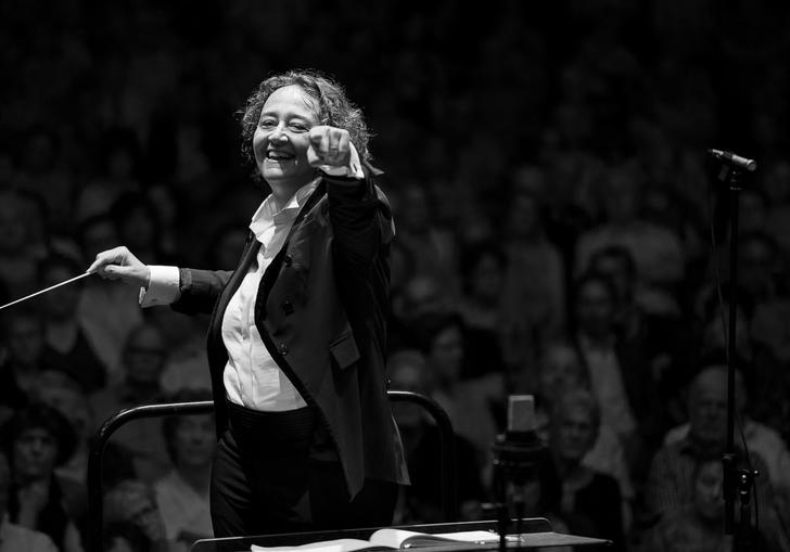 An image of Nathalie pointing at the camera joyfully whilst conducting in a recent concert