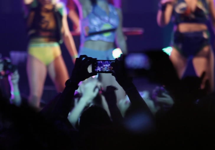 a person in a crowd holds their phone up to film the girl band on stage