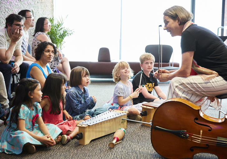 A Member of the LSO talks to a group of children. The have a cello and percussion instrumnets to try.
