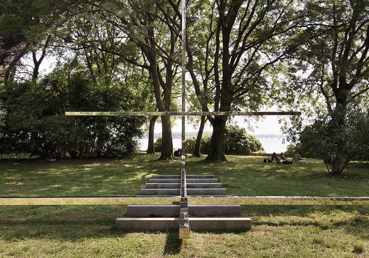 A big cross structure made from a reflective mirror like material in a nice green park by architect Carla Juaçaba