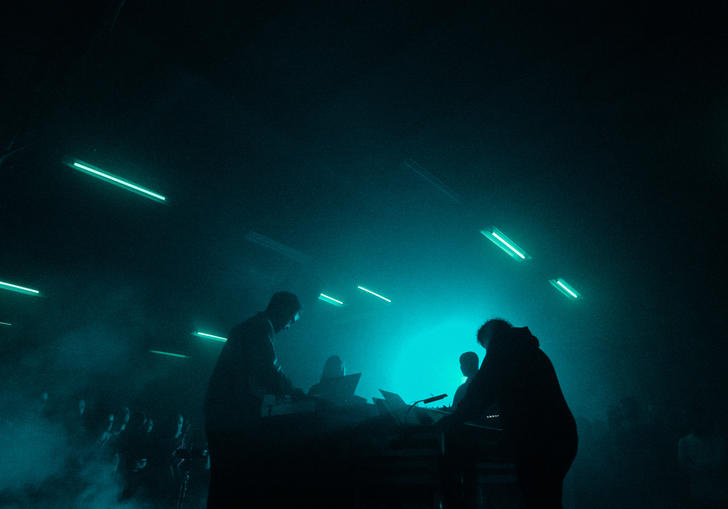 A live performance featuring four musicians facing each other with smoke and stobe lights around them