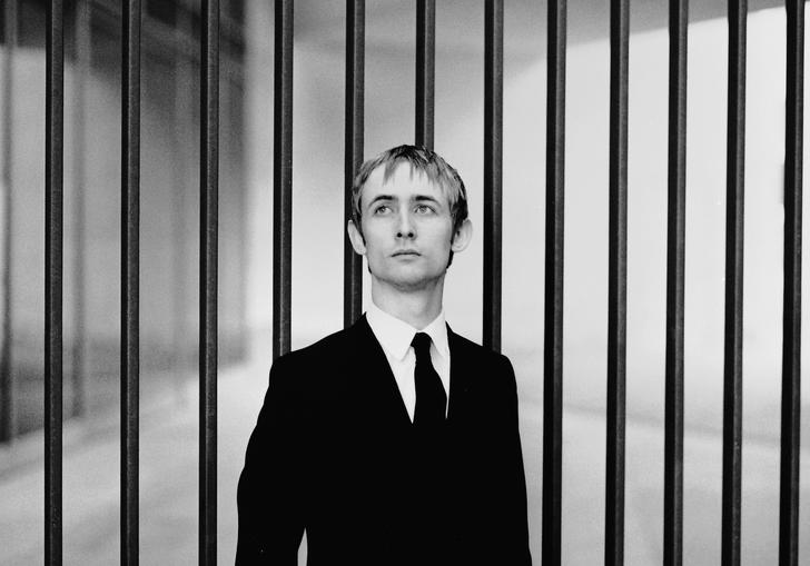 black and white photo of Neil Hannon wearing a suit against a backdrop of vertical bars