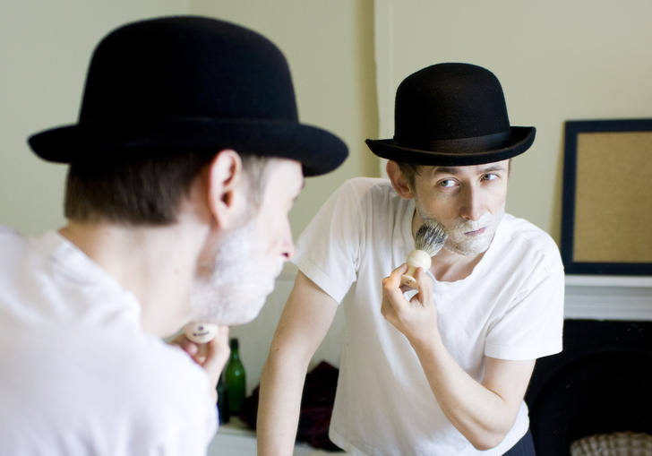 Colour photo of Neil Hannon wearing a bowler hat, shaving with foam on his face