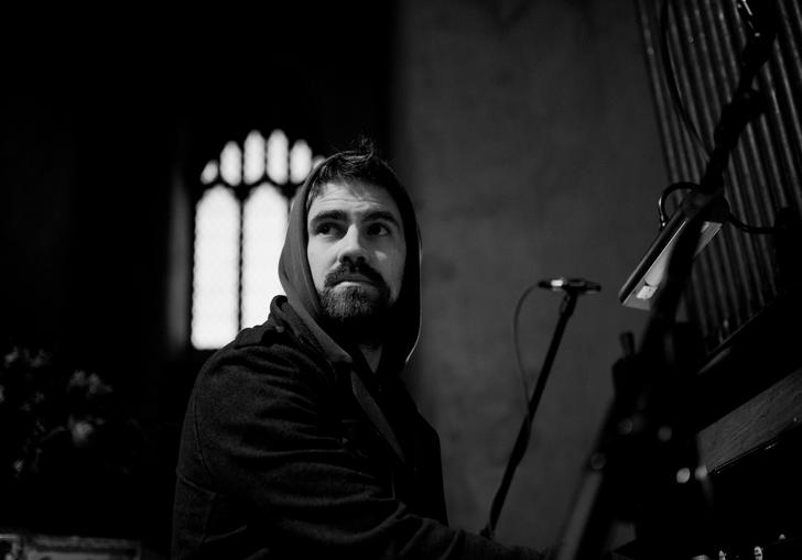 black and white image of Kit Downes playing the organ with an arched church window in the background