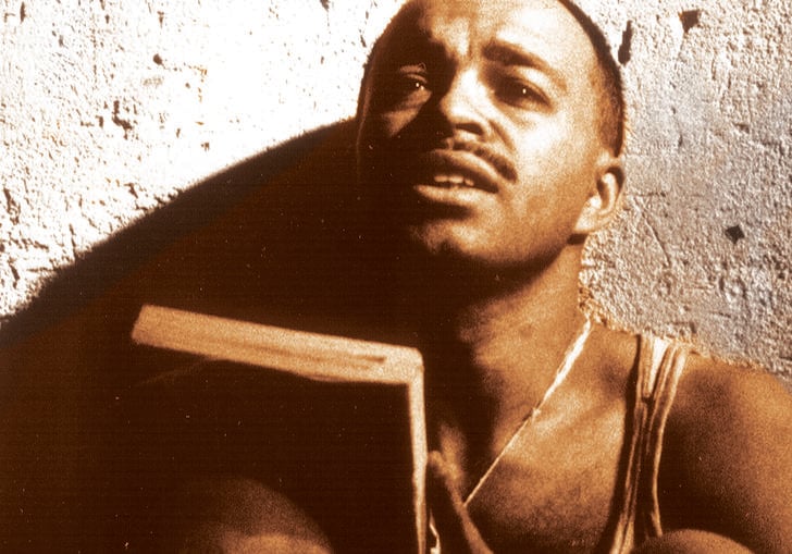 A man sat against a wall holding a book