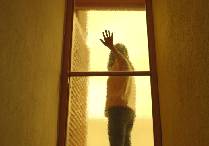 orange tinted image of a person behind glass with a hand of the glass