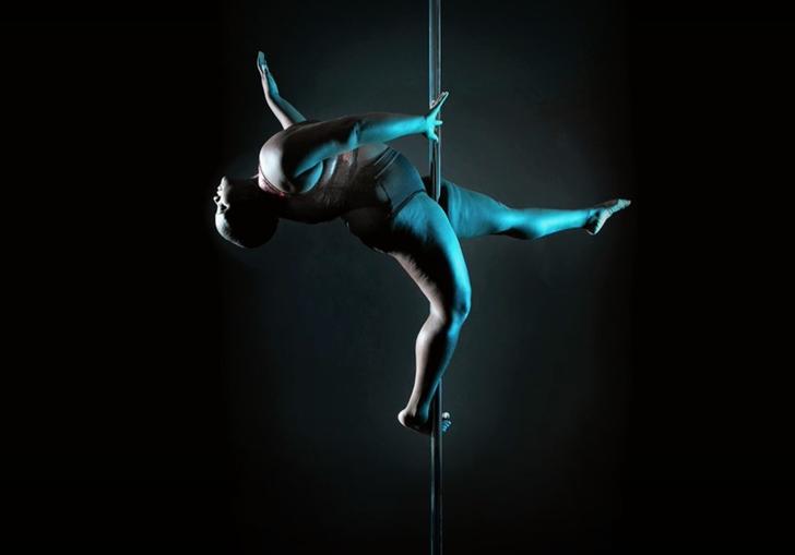a fat black dances on a pole in darkness, lit by a blue light