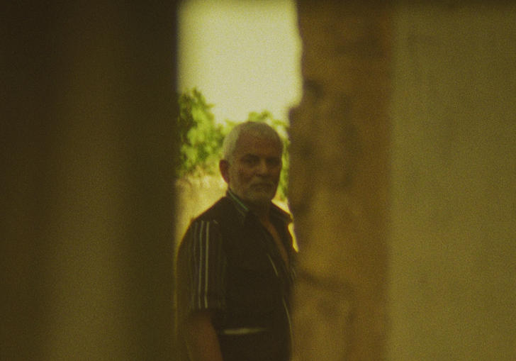 An older man looks through a gap in two walls