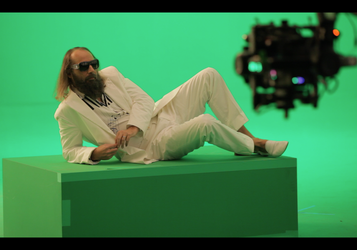 Sebastian Tellier reclines in a white suit against a green screen