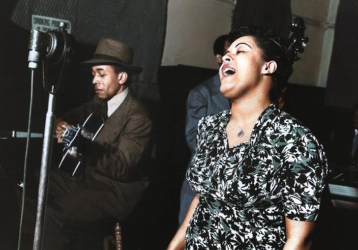 a woman singing and a man sitting next to her playing a guitar