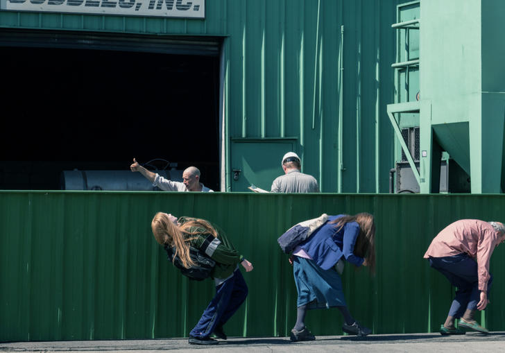 a man an two women hunch down so they can't be seen walking past a fence