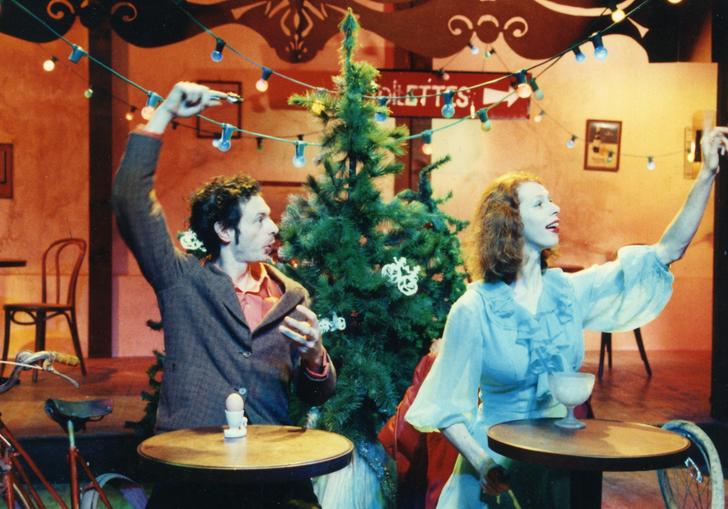 A man and woman sit at individual mini tables in front of a Christmas tree