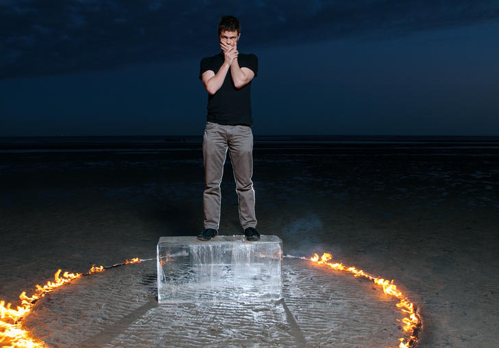 David Finnegan stands on an ice block, in a desert. A ring of fire burns around him.