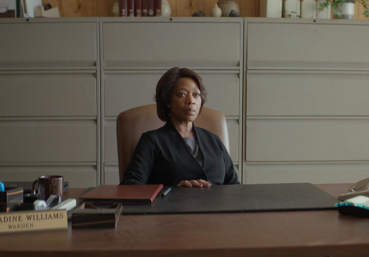 Alfre Woodard sits behind a big desk wearing a suit