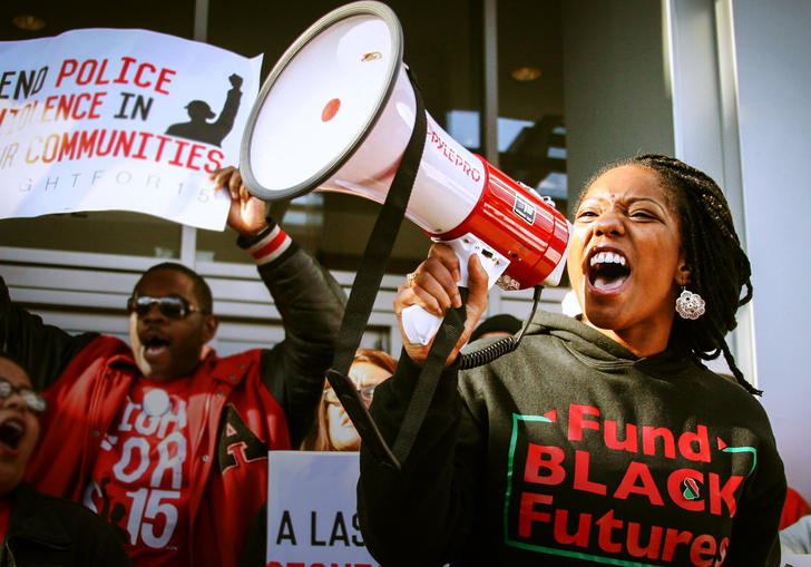 activists wearing BLM jumpers hold up signs and shout into a megaphone