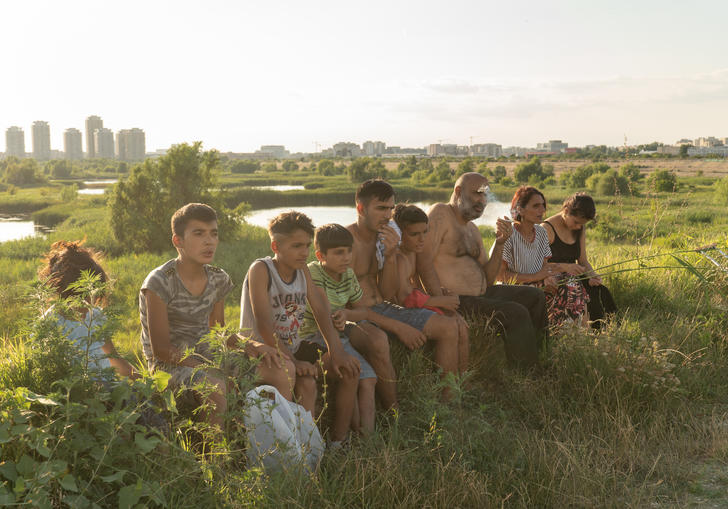 A family sit in a row surrounded by a green field, with a city visible in the distance