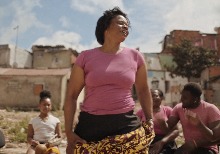 A woman in a pink t-shirt dances with a scarf, among other musicians 