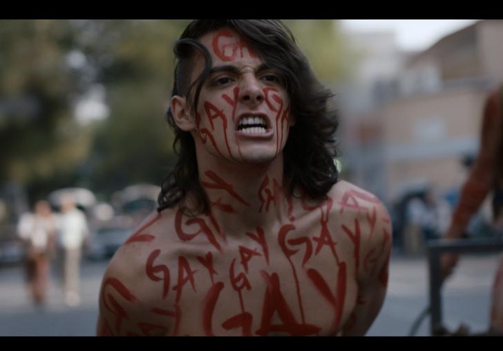 a man covered in red writing protests on the street