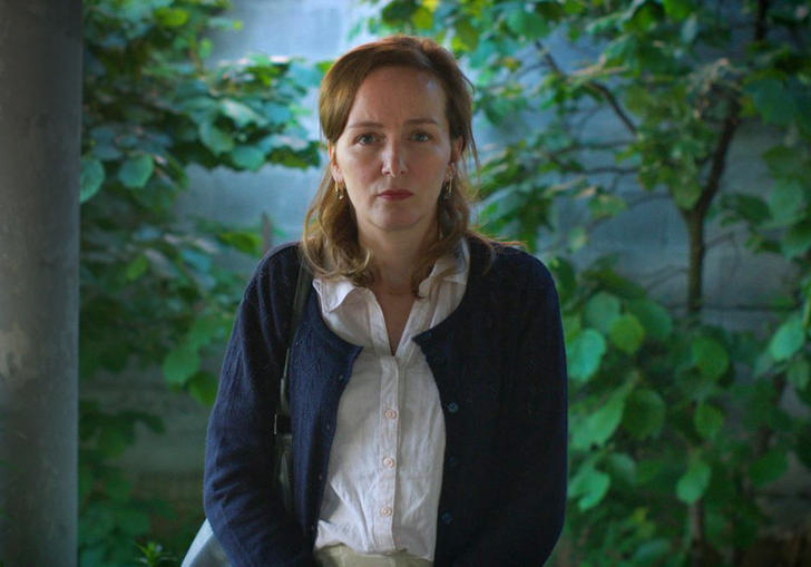 a woman stands looking past the camera with green in the background