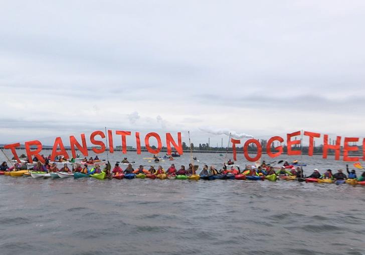 climate activists tie themselves together in kayaks holding a sign that says 'transition together'