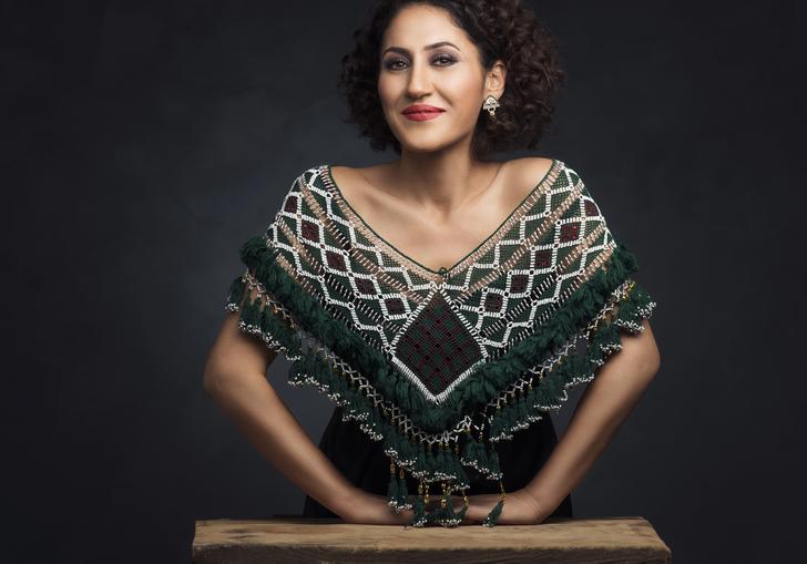 Aynur wearing an embroidered shawl leaning on a small wooden table