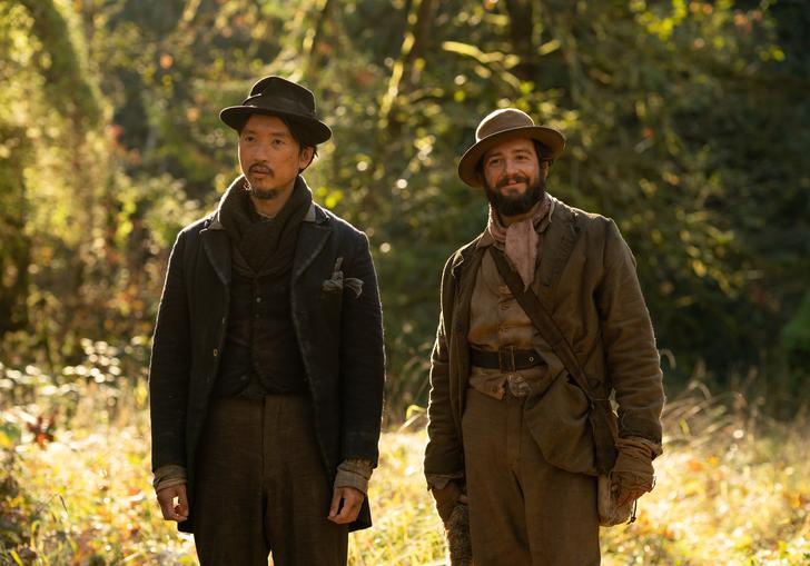 two men stand next to each other surrounded by wilderness