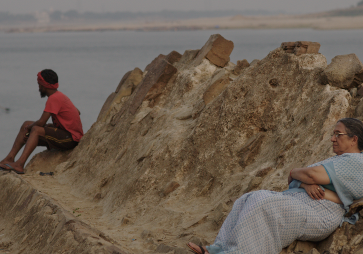 an older woman and younger man sit on a rock