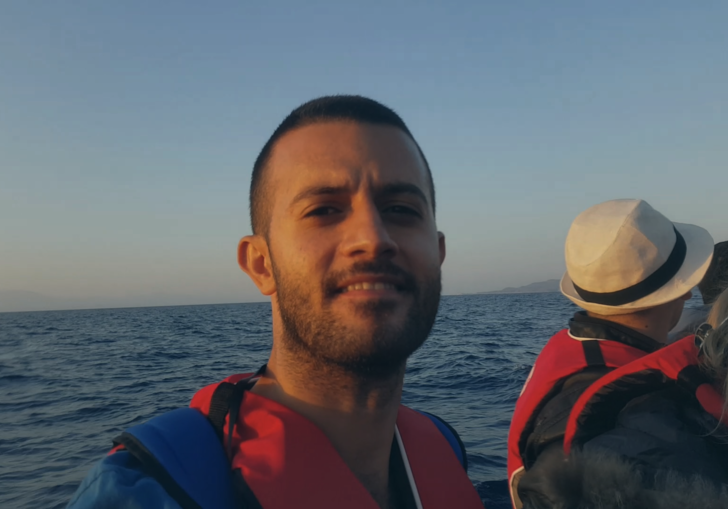 a man looks into the camera wearing a life vest and sitting on a boat