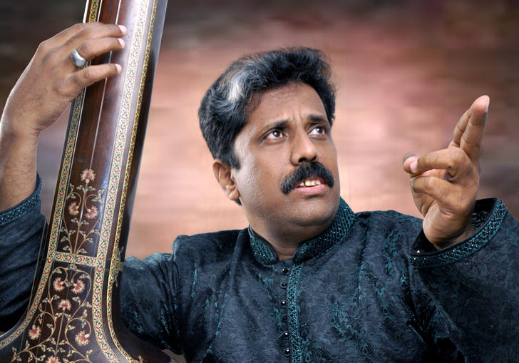 Waseem Ahmed Khan posing with his sitar, pointing to his left