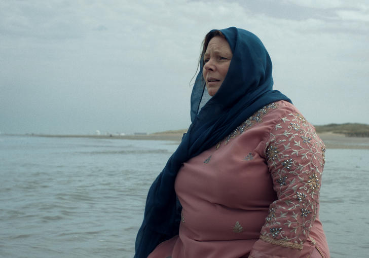 a woman wearing a hijab stands on the cliffs looking out to sea