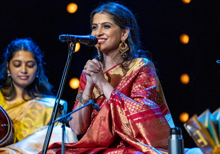 Kaushiki Chakraborty sitting at a microphone, smiling with her hands clasped together