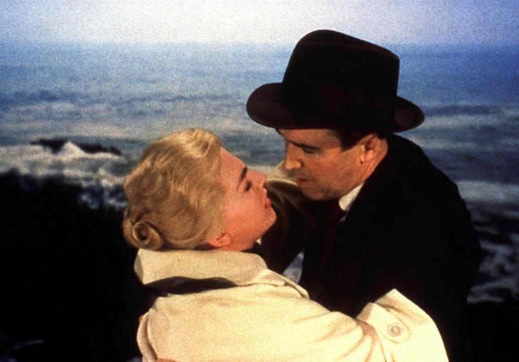 Kim Novak in a white coat and James Stewart in a black suit and hat embrace, in Alfred Hitchcock's Vertigo