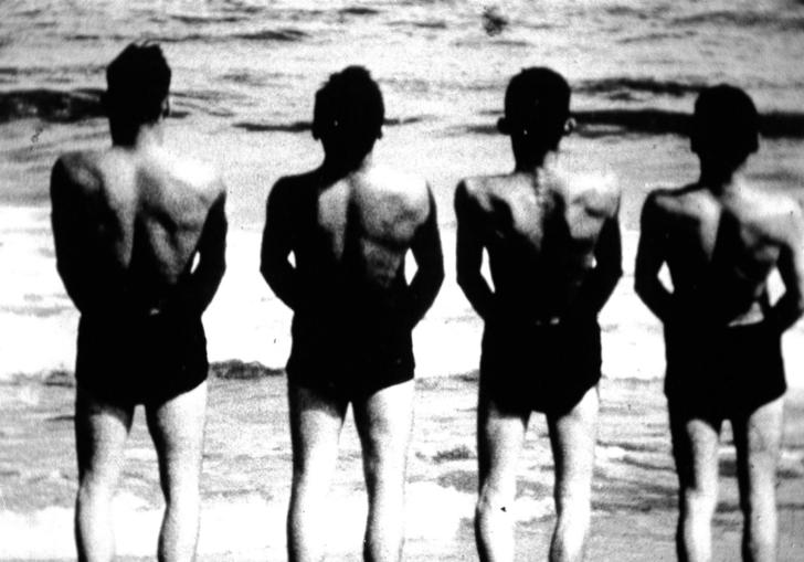 four men line up facing the sea with their backs to the camera