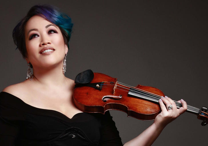 LSO First Violin Maxine Kwok smiles, holding a violin against a dark background