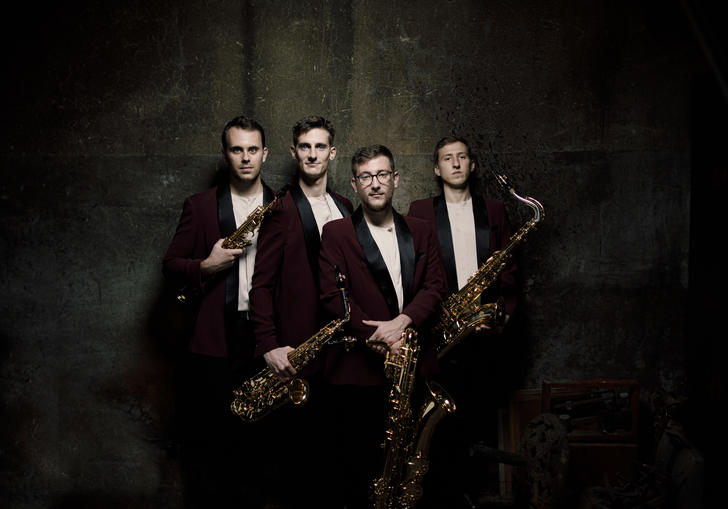 The Kebyart Ensemble stand holding their saxophones, looking at the camera