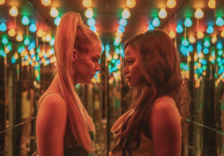 two women stand opposite each other is a room full of coloured lights