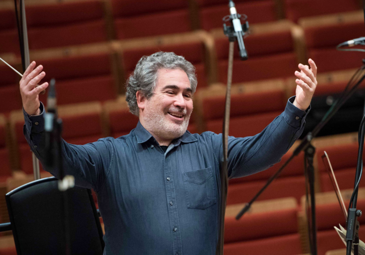 Carlo Rizzi smiles with his arms up, conductor's baton in his right hand