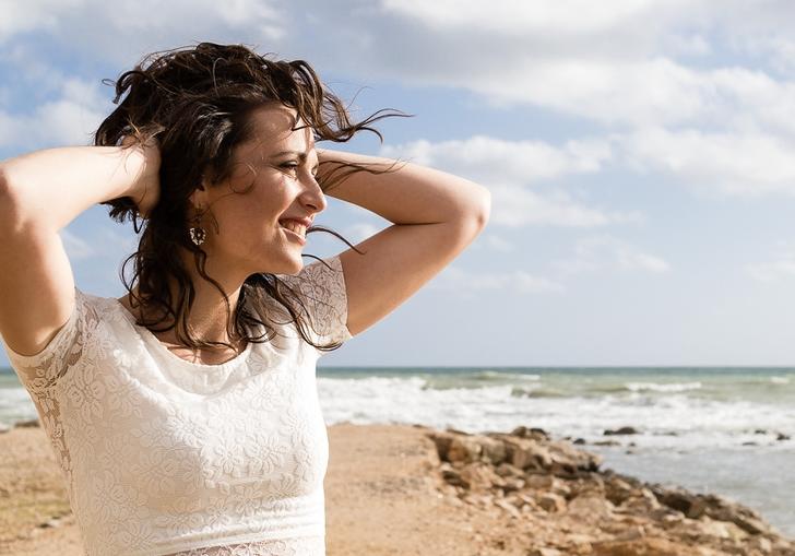 Noemi Nuti on a beach wearing a white t shirt, with both hands on her head