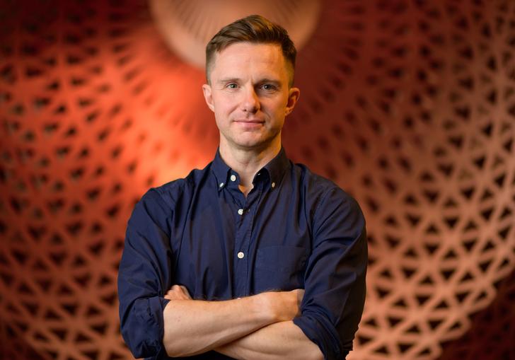 James McVinnie stands in front of a big orange dome, with his arms crossed