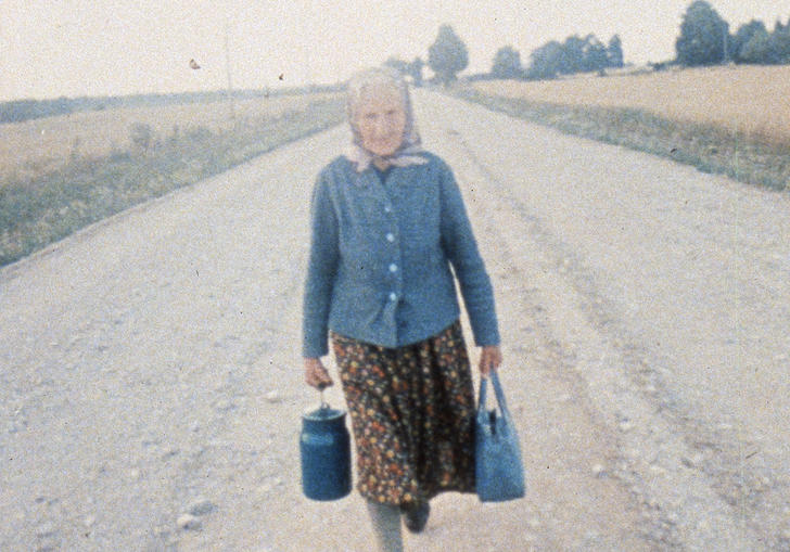 An elderly woman walks along an empty rural road in Jonas Mekas' Reminiscenes of a Journey to Lithuania
