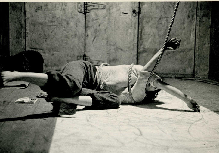 An image of Carolee lying on the floor with her arms tied up in some rope 