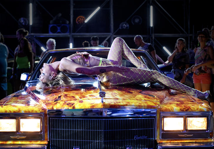 Woman in fishnet lingerie lounging on the hood of a car