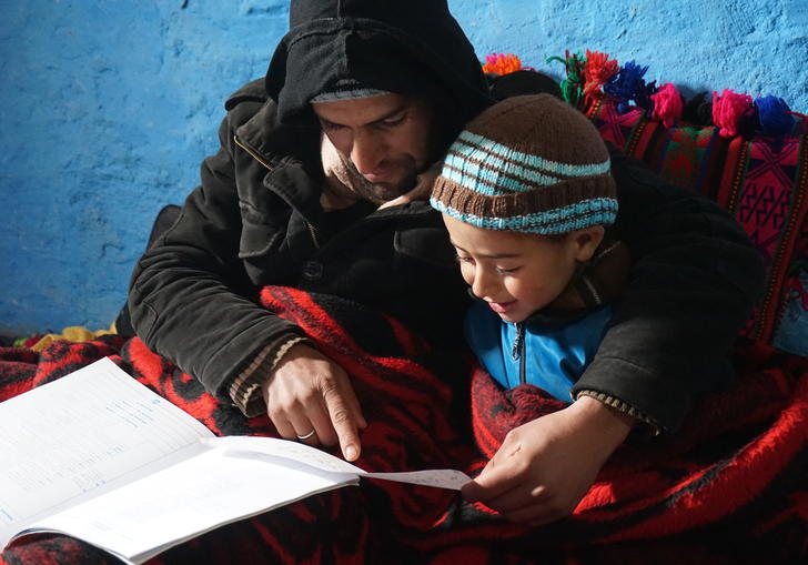 An older man reads to a young boy covered in red blankets