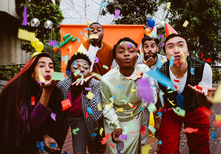 The PappyShow performers blow multi coloured confetti through the air towards the camera. 