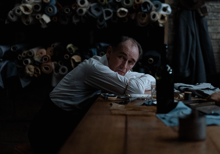 Mark Rylance leaning on a fabric cutting table